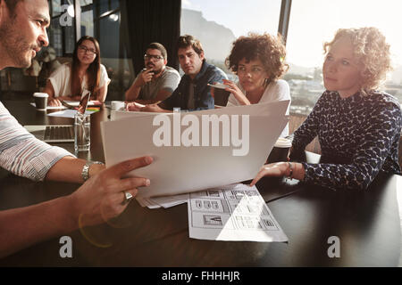 Closeup shot of team of young people going over paperwork. Creative people meeting at restaurant table. Focus on hands and docum Stock Photo