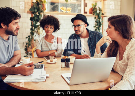Portrait of young people sitting around in cafe with a laptop. Creative team meeting in a coffee shop for discussing new busines Stock Photo