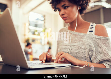 Portrait of young woman looking busy working on laptop at a cafe. African woman sitting in coffee shop using laptop. Stock Photo