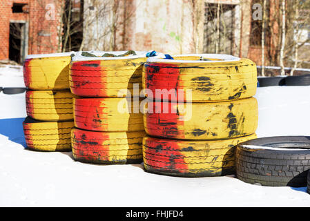 Three stacks of red and yellow painted car tires on the turn of a karting racing track. Some snow cover the track and industrial Stock Photo