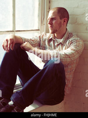 A pensive looking man sitting on a window ledge Stock Photo