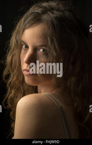 Unretouched photo of fair-skinned woman with wavy/curly brown hair, blue eyes and serious expression in dramatic studio lighting Stock Photo