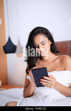 Hispanic woman using her hand-held device in her hotel bedroom Stock Photo