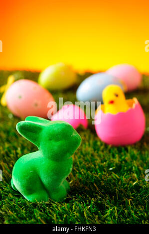 closeup of a green easter rabbit on the grass with some colorful decorated eggs and a toy chick emerging from a pink egg in the Stock Photo