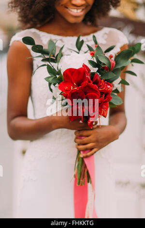 Charming african bride holds in hands bouquet of red flowers Stock Photo