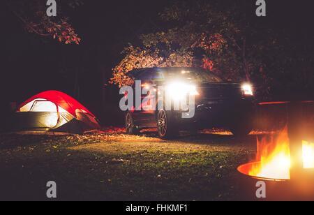 Camping Adventure. Tent Camping in the Deep Forest. Modern Offroad Car, Tent and Burning Wood in the Camping Fire Pit. Stock Photo