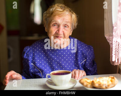 An elderly woman sitting in the kitchen drinking tea. Stock Photo