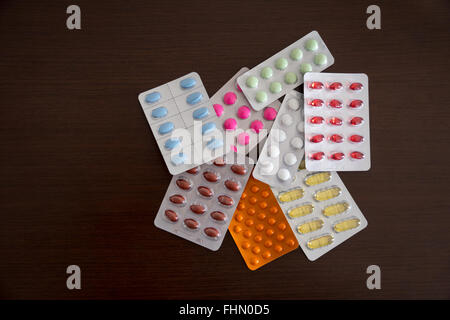 Heap of packs of pills and capsules (white, blue, green, yellow, orange, pink, red, wine-colored) on brown wooden background Stock Photo