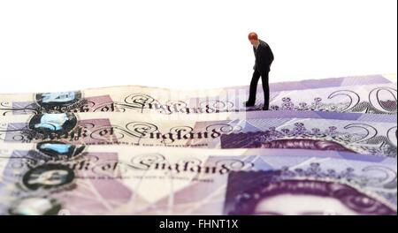 A miniature figurine business man in a suit looking down at the words Bank Of England on some twenty pound notes Stock Photo