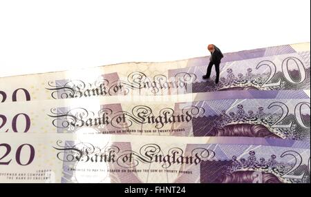 A miniature figurine business man in a suit looking down at the words Bank Of England on some twenty pound notes Stock Photo