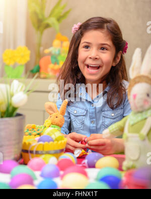 Portrait of cute little girl playing in daycare, painting eggs in different colors, with pleasure preparing to happy Easter Stock Photo