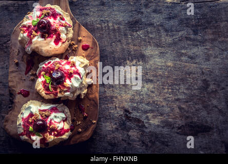 Served meringues pavlova cake with fresh cherry sauce on wooden background with blank space Stock Photo