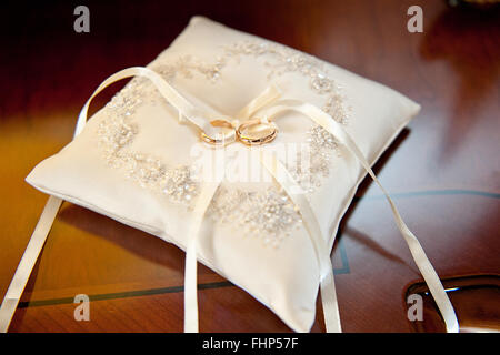 Two amazing golden shiny rings jewel for nuptials ceremony laying on white beautiful pillow with bow Stock Photo