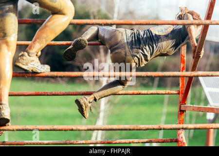 Participants in extreme obstacle race climbing over hurdle Stock Photo