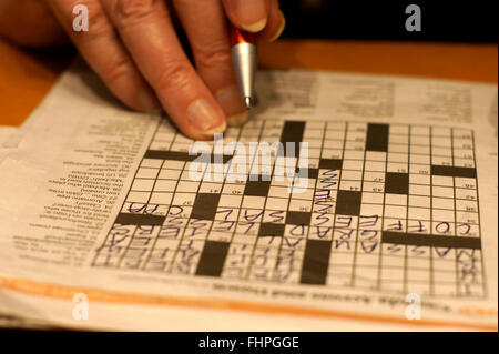 Closeup of a woman's hand, pen, and newspaper crossword puzzle Stock Photo
