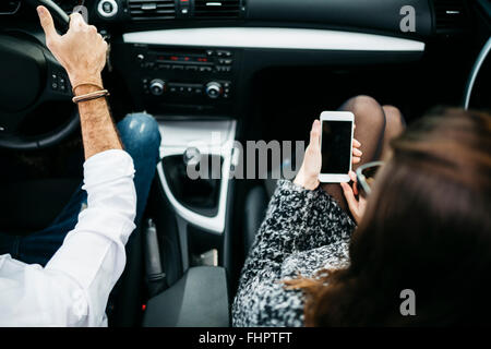 Young couple driving in a car, co driver using smart phone Stock Photo
