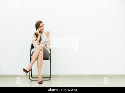 woman in office outfit sitting in a chair with and talking relaxed at cellphone Stock Photo