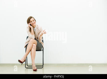 woman in office outfit sitting in a chair with and talking relaxed at cellphone Stock Photo