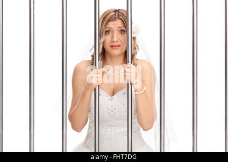 Worried young bride standing behind bars in jail isolated on white background Stock Photo