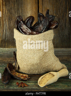 Carob pods in linen bag on wooden background Stock Photo
