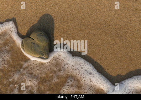 Heart shaped rock washed by the sea on a sandy beach. Stock Photo