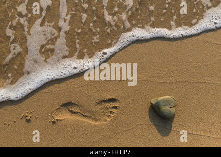Heart shaped rock washed by the sea on a sandy beach. Stock Photo