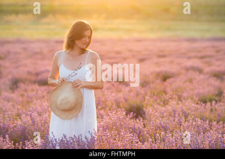 Beautiful young woman wearing a white dress standing in a moment of peace and serenity  in a middle of a lavender field under th Stock Photo