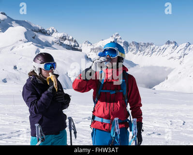 Two skiers having a snack eating a banana and drinking from a water bottle whilst skiing on ski slopes in French Alps. Flaine Rhone-Alpes France EU Stock Photo