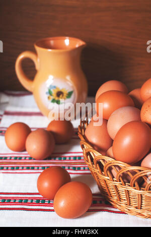 Beautiful fresh eggs in a basket on a woven background with a clay jar. Easter, diet and nutrition stock image Stock Photo