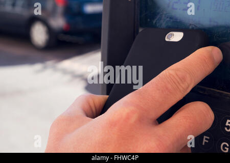 closeup of a young caucasian man using his smartphone to pay via contactless in a parking meter Stock Photo