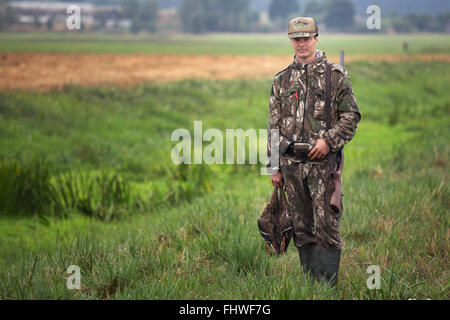 Hunter in camouflage with shotgun holding ducks in hand. Man hunting ducks Stock Photo