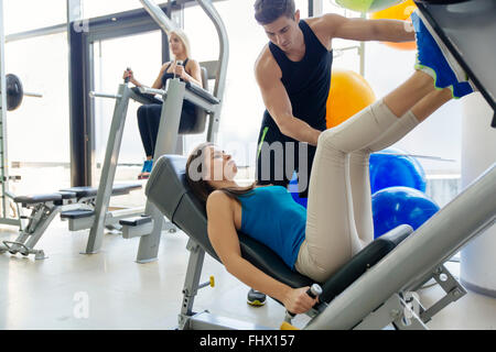 Beautiful woman doing leg exercises in gym with the help of personal trainer Stock Photo