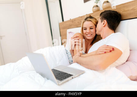 Couple with laptop in bed reading news and smiling Stock Photo