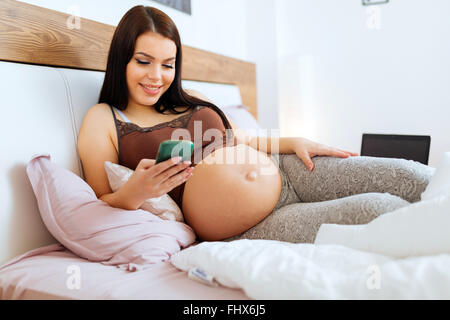 Pregnant woman using phone while lying on bed and resting Stock Photo