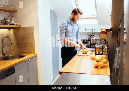 Man slicing oranges in kitchen with knife Stock Photo