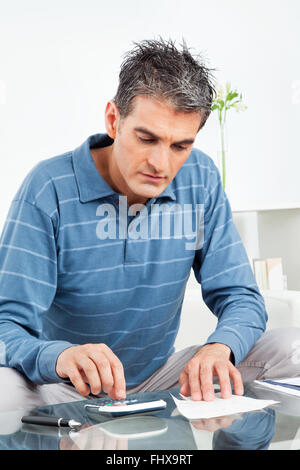 Man with calculator and bills on living room table Stock Photo