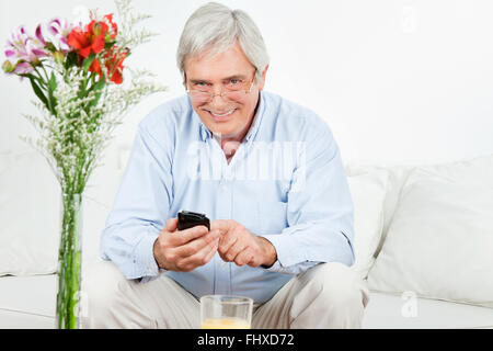 Happy senior man using a smartphone on the couch Stock Photo