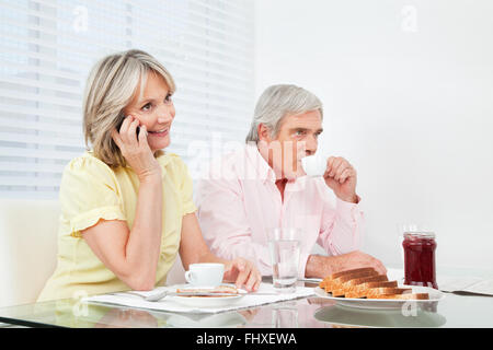 Senior woman using her cell phone at breakfast table Stock Photo