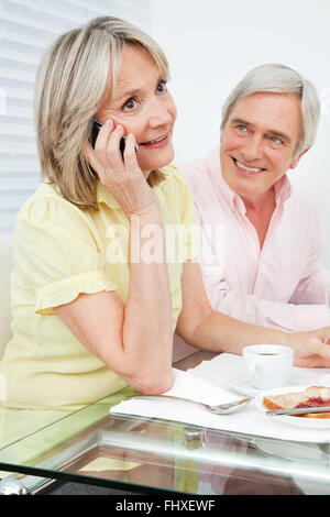 Senior woman talking to cell phone at breakfast table Stock Photo