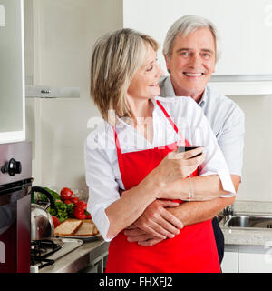 Happy senior husband embracing smiling wife in kitchen Stock Photo