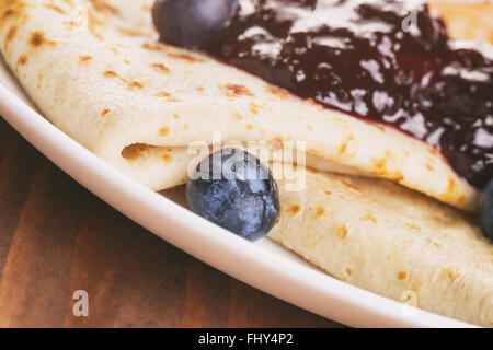 homemade blinis or crepes with blueberries and jam on wooden table Stock Photo