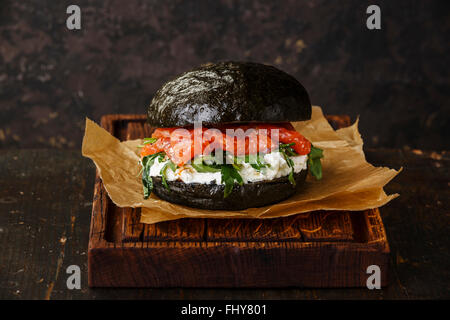 Black Salmon burger with cream cheese and arugula on dark wooden background Stock Photo