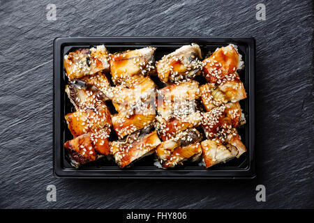 Eel Sushi rolls in plastic box packaging tray on black stone slate background Stock Photo