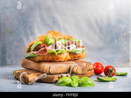 Croissant sandwich with smoked meat Prosciutto di Parma sun dried tomatoes fresh spinach and basil on stone textured grey back Stock Photo