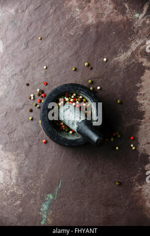Mortar and pestle with multicolored pepper on stone slate background Stock Photo
