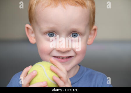 Red Haired, blue eyed Boy Close Up, smiling and holding a tennis ball shot close up Stock Photo