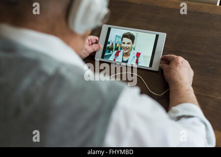 Senior man using mini tablet and headphones for skyping with his grandson Stock Photo
