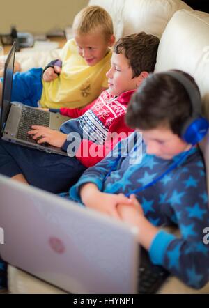 MODEL RELEASED. Three boys using laptops sitting on the sofa. Stock Photo
