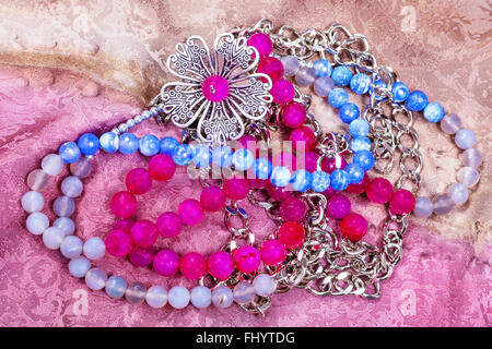 tangled necklace from natural gemstones (pink, blue, smoky agate and hematite beads) with metal flower on painted textile backgr Stock Photo
