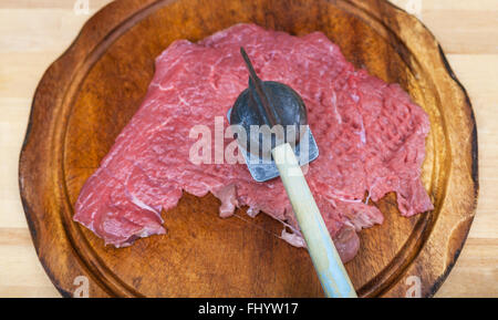top view of slice of raw veal is beating by meat tenderizer on cutting board Stock Photo